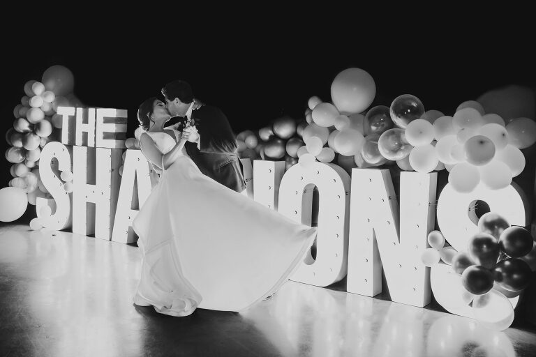 bride and groom kiss in front of lighted sign