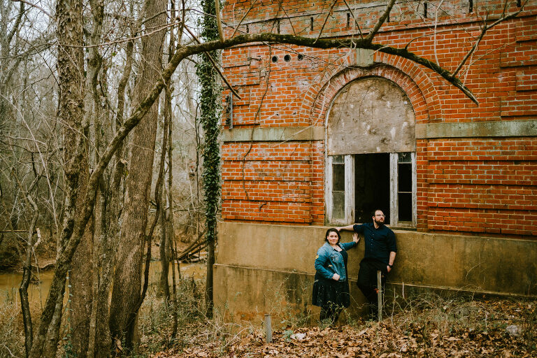 couple posing on the side of a brick building in the woods
